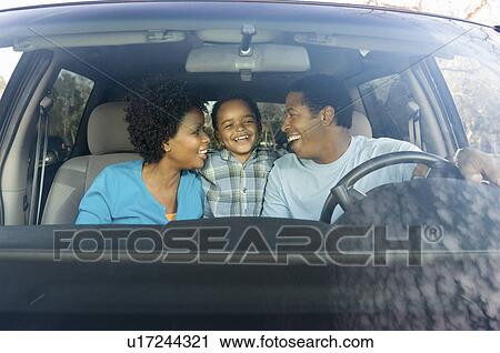 Stock Image - Couple smiling at young son in car, view through windscreen. Fotosearch