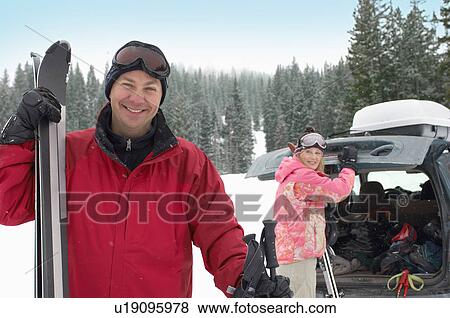 Couple standing in snow with skis, woman opening trunk of car. View Large Photo Image Stock Photo - Couple standing in snow with skis, woman opening trunk of car.. Fotosearch