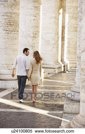 Stock Photography - Couple walking between pillars, Rome, Italy, back view. Fotosearch