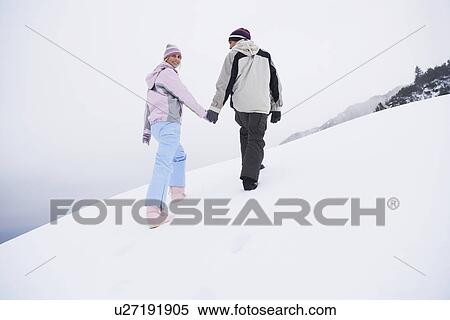 Stock Photography - Couple walking up snow-covered hill, back view, low angle view. Fotosearch