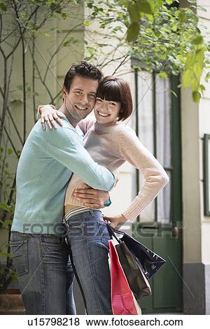 Couple with shopping bags embracing in front of building View Large Photo Image Stock Photo - Couple with shopping bags embracing in front of building. Fotosearch