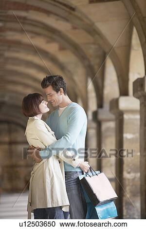 Couple with shopping bags embracing under archway View Large Photo Image Stock Image - Couple with shopping bags embracing under archway. Fotosearch