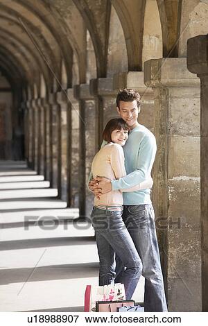 Stock Photo - Couple with shopping bags embracing under archway. Fotosearch