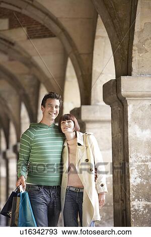 Stock Image - Couple with shopping bags walking through archway. Fotosearch