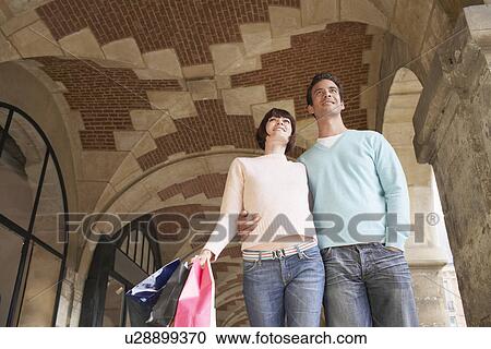 Stock Image - Couple with shopping bags walking through archway. Fotosearch