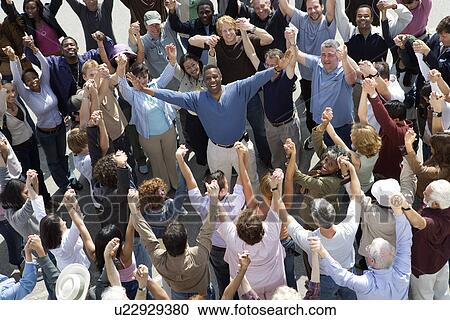 Stock Image - Crowd with arms raised surrounding man. Fotosearch