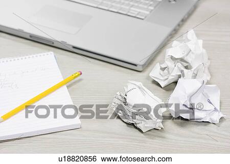 Stock Photograph - Crumpled paper and notebook on desk by laptop, close up. Fotosearch