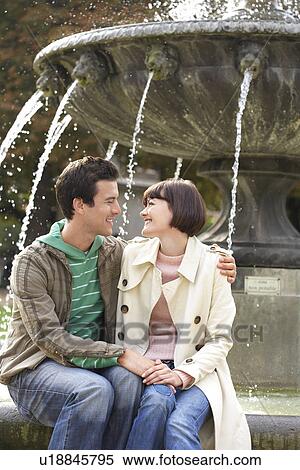 Stock Photography - Embracing couple sitting on edge of fountain. Fotosearch