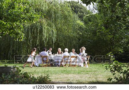 Stock Image - Family eating at table in garden. Fotosearch