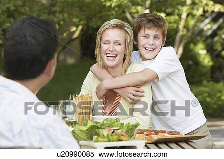 Stock Photography - Family eating meal outside, son hugging mother. Fotosearch
