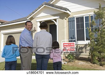Stock Image - Family with two children (6-8) in front of new house, back view. Fotosearch