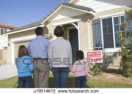 Stock Image - Family with two children (6-8) in front of new house, back view. Fotosearch