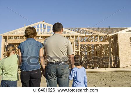Stock Photograph - Family with two children (6-9) at construction site, back view. Fotosearch