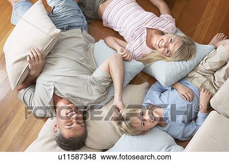 Stock Photo - Father and Children Lying on pillows and cushions on wood Floor, overhead view. Fotosearch