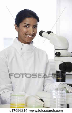 Picture - Female Asian lab worker standing by microscope. Fotosearch