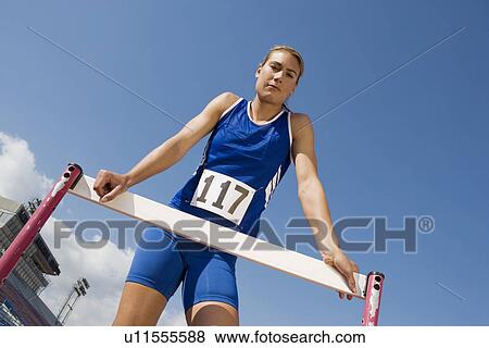 Stock Photo - Female athlete with hurdle, low angle view. Fotosearch