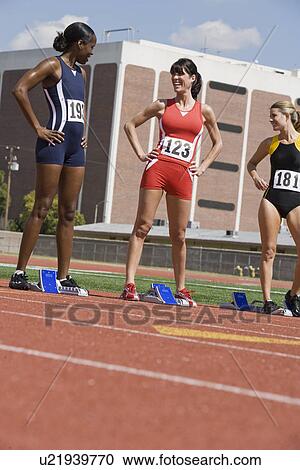 Stock Image - Female athletes next to starting blocks, chatting. Fotosearch
