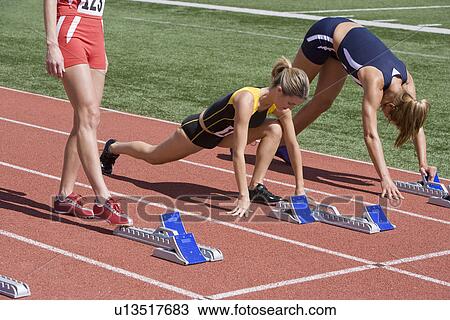 Stock Image - Female athletes warming up next to starting blocks. Fotosearch