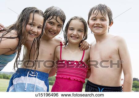 Stock Photograph - Four wet children in swimsuits standing in field, portrait. Fotosearch