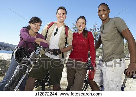 Picture - Four young adults, standing on lake shore, with mountain bikes.. Fotosearch
