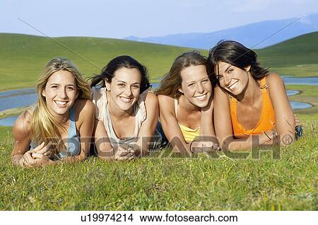 Four young woman lying near mountain lake, portrait, ground view View Large Photo Image Picture - Four young woman lying near mountain lake, portrait, ground view. Fotosearch