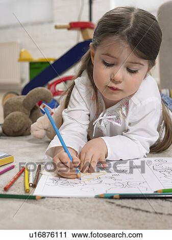 Stock Image - Girl (3-4) with colouring book on floor in home. Fotosearch