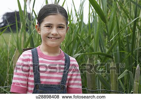 Stock Photo - Girl (5-6) standing beside reeds, portrait. Fotosearch