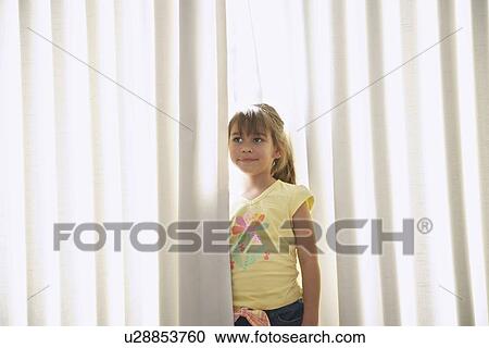 Stock Image - Girl (5-6) standing between blinds. Fotosearch