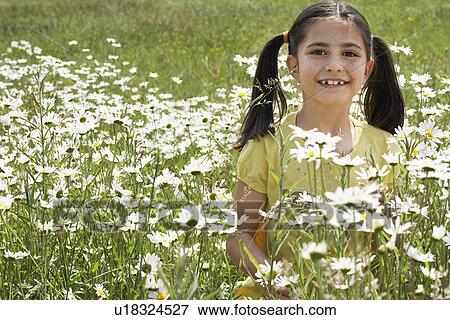 Stock Photo - Girl (7-9) holding flowers in meadow, portrait. Fotosearch