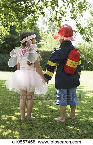 Stock Photograph - Girl and boy standing in park dressed up as fairy and fireman. Fotosearch