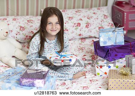 Girl sitting in bed holding christmas presents, portrait View Large Photo Image Stock Image - Girl sitting in bed holding christmas presents, portrait. Fotosearch