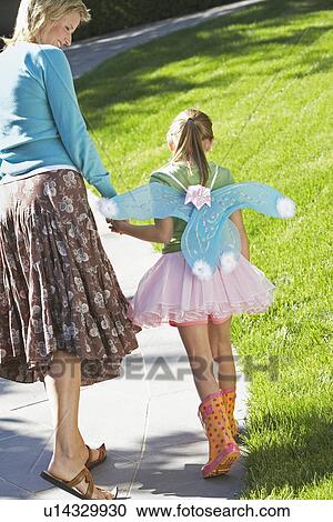 Stock Image - Girl wearing fairy wings and tutu walking with mother on park path, back view. Fotosearch