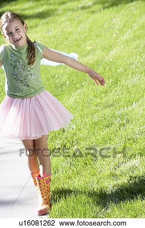 Stock Image - Girl wearing fairy wings and tutu balancing on edge of path, portrait. Fotosearch