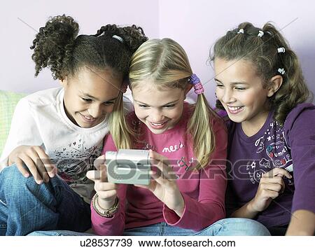 Girls sitting side by side playing with electrical gadget View Large Photo Image Stock Photo - Girls sitting side by side playing with electrical gadget. Fotosearch