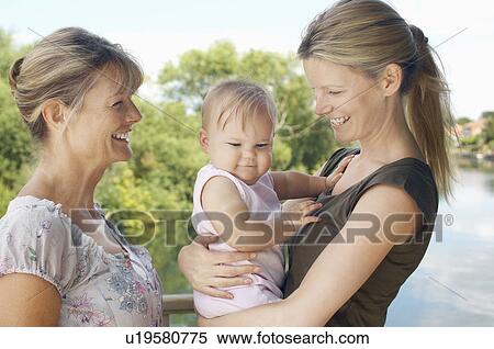 Stock Photography - Grandmother, mother and daughter by lake, half length. Fotosearch