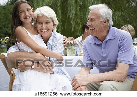 Stock Photograph - Grandparents with granddaughter (10-12) sitting at table in garden. Fotosearch