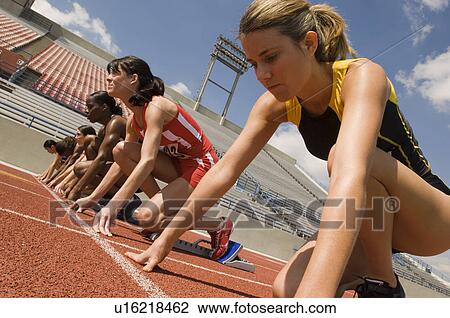 Stock Image - Group of female track athletes on starting blocks. Fotosearch