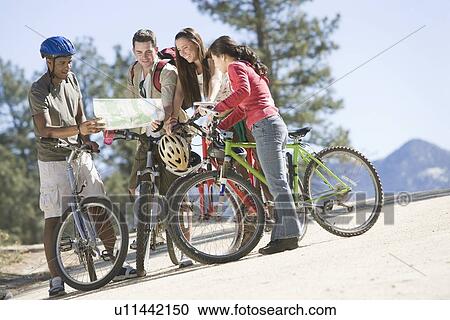 Stock Image - Group of friends looking at map on cycling holiday. Fotosearch