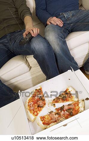 Stock Photo - Half eaten pizza in box by people on sofa, low section. Fotosearch
