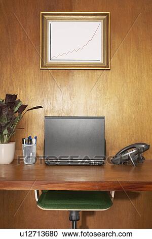 Stock Image - Laptop and other items on desk, framed graph above desk. Fotosearch