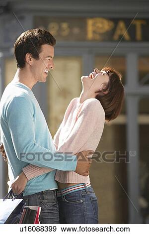 Laughing couple embracing in front of shop View Large Photo Image Stock Photo - Laughing couple embracing in front of shop. Fotosearch