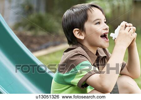 Stock Photograph - Little boy on slippery slide in park using inhaler. Fotosearch