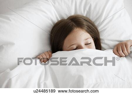 Stock Photo - Little girl in bed with covers pulled up over face,, close up, high angle view. Fotosearch