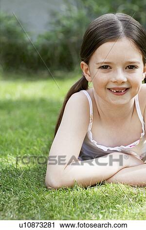 Stock Image - Little Girl Lying in Grass in backyard, portrait. Fotosearch