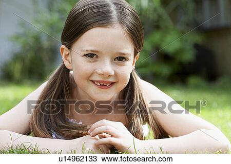 Stock Image - Little Girl Lying in Grass in backyard, portrait. Fotosearch