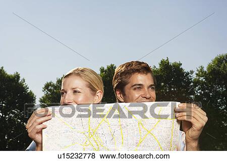 Lost smiling young couple in park holding map View Large Photo Image Stock Photo - Lost smiling young couple in park holding map. Fotosearch