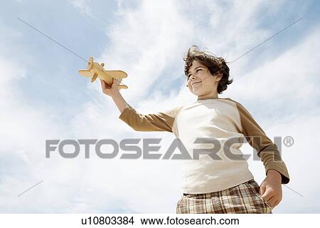 Picture - Low angle view of boy holding up wooden toy airplane against blue sky. Fotosearch
