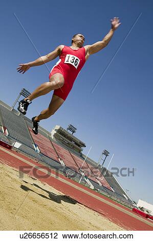Stock Image - Male athlete long jumping, mid-air. Fotosearch
