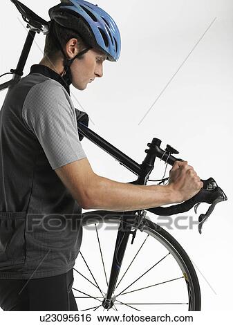 Stock Photograph - Male bicyclist carrying bicycle, side view. Fotosearch