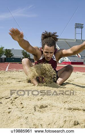 Stock Image - Male long jumper landing in sand pit. Fotosearch